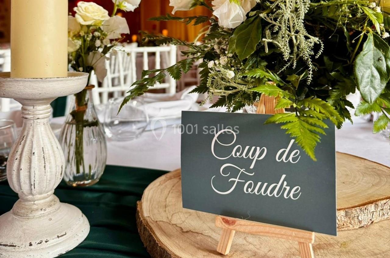 Location salle La Chapelle-Gauthier (Seine-et-Marne) - Nomade-Lodge #47 Carte ’Coup de Foudre’ posée sur un chevalet en bois, entourée de fleurs et d'une bougie sur une table décorée.
