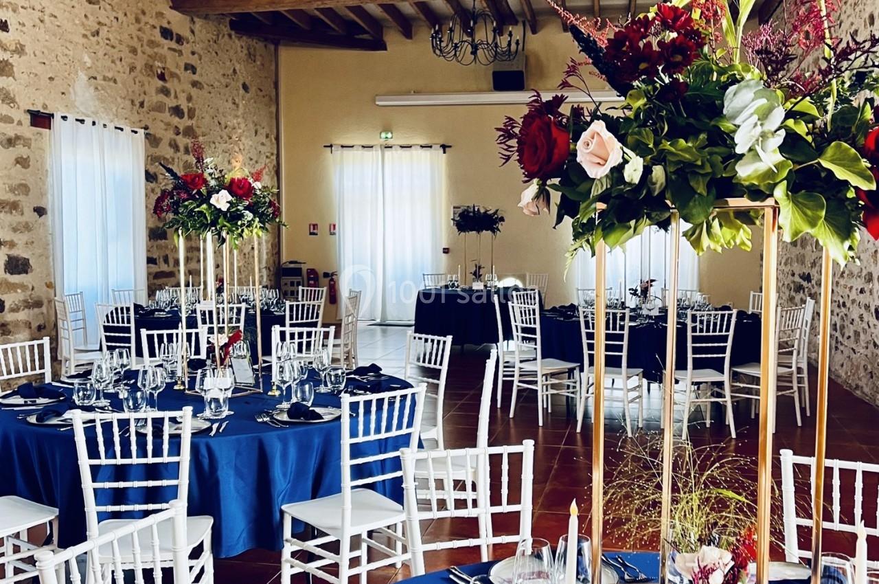 Location salle La Chapelle-Gauthier (Seine-et-Marne) - Nomade-Lodge #48 Salle de réception décorée avec des tables rondes, nappes bleues, chaises blanches et centres de table fleuris.