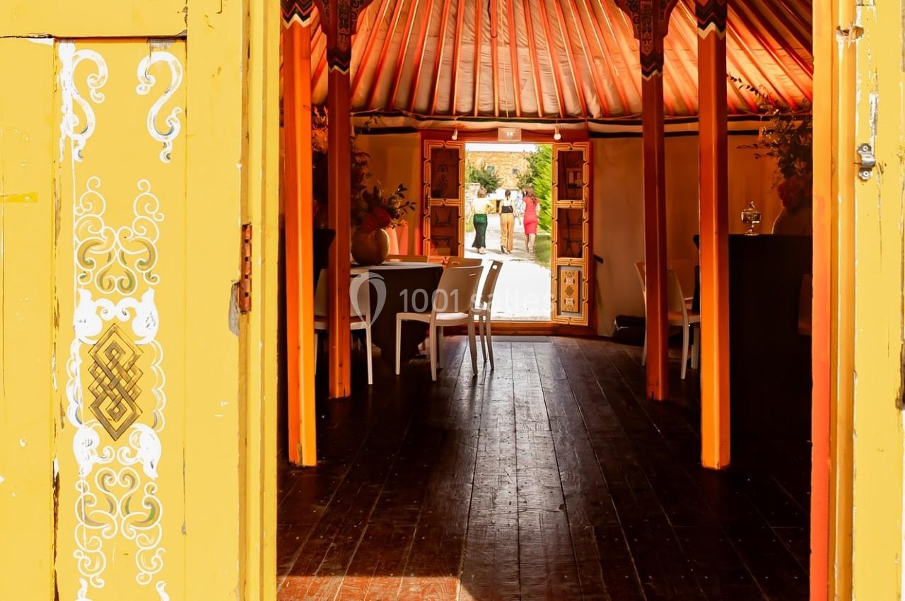 Location salle La Chapelle-Gauthier (Seine-et-Marne) - Nomade-Lodge #51 Vue intérieure d'une tente colorée avec des tables et des chaises, ouverte sur un jardin ensoleillé à l'arrière-plan.