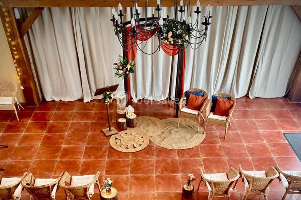 Location salle La Chapelle-Gauthier (Seine-et-Marne) - Nomade-Lodge #54 Salle décorée pour une cérémonie avec chaises en rotin, tapis, fleurs et un lustre suspendu au plafond.