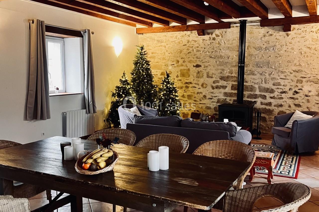 Location salle La Chapelle-Gauthier (Seine-et-Marne) - Nomade-Lodge #57 Salle de séjour chaleureuse avec murs en pierre, poêle à bois, sapins décorés et table en bois avec des bougies.
