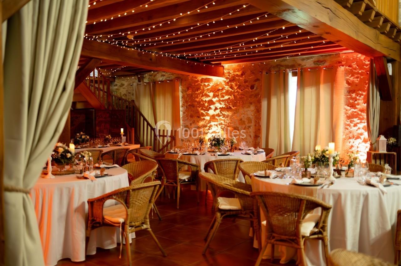 Location salle La Chapelle-Gauthier (Seine-et-Marne) - Nomade-Lodge #61 Salle de réception chaleureuse avec tables rondes décorées, chaises en rotin et éclairage tamisé sous un plafond en bois.