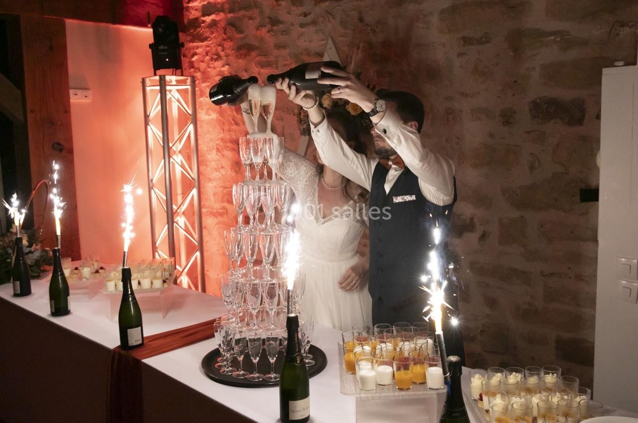 Location salle La Chapelle-Gauthier (Seine-et-Marne) - Nomade-Lodge #62 Un couple remplit une pyramide de coupes de champagne lors d'une réception, entouré de décorations festives.