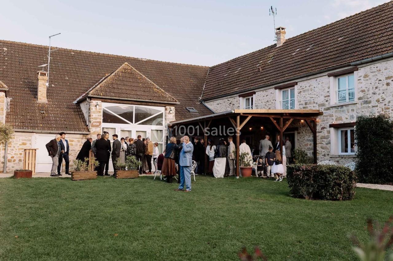 Location salle La Chapelle-Gauthier (Seine-et-Marne) - Nomade-Lodge #65 Groupe de personnes rassemblées dans une cour devant une grande maison en pierre avec un jardin bien entretenu.
