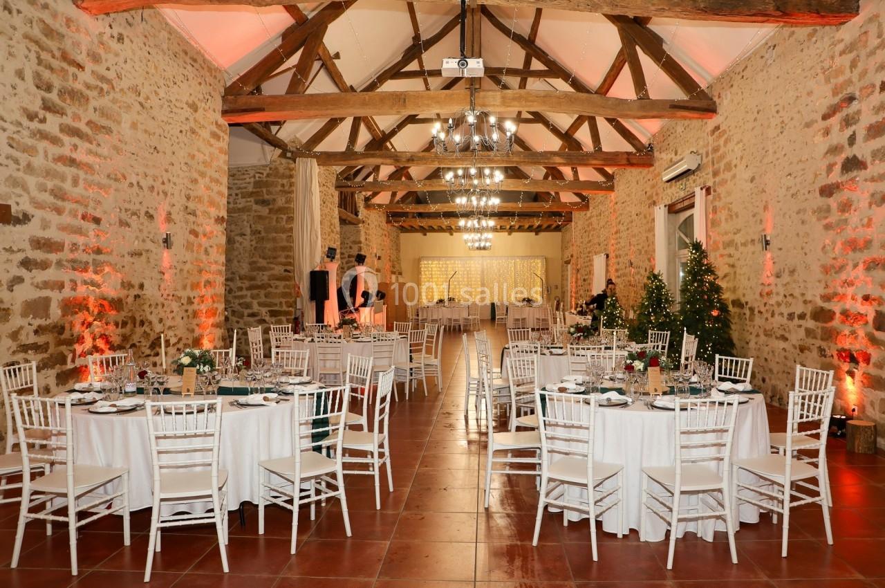 Location salle La Chapelle-Gauthier (Seine-et-Marne) - Nomade-Lodge #73 Salle de réception en pierre avec poutres apparentes, tables rondes dressées et décorations lumineuses.