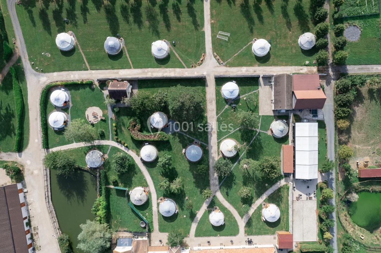 Location salle La Chapelle-Gauthier (Seine-et-Marne) - Nomade-Lodge #75 Vue aérienne d'un site avec des yourtes blanches réparties dans un espace vert aménagé avec chemins et bâtiments.