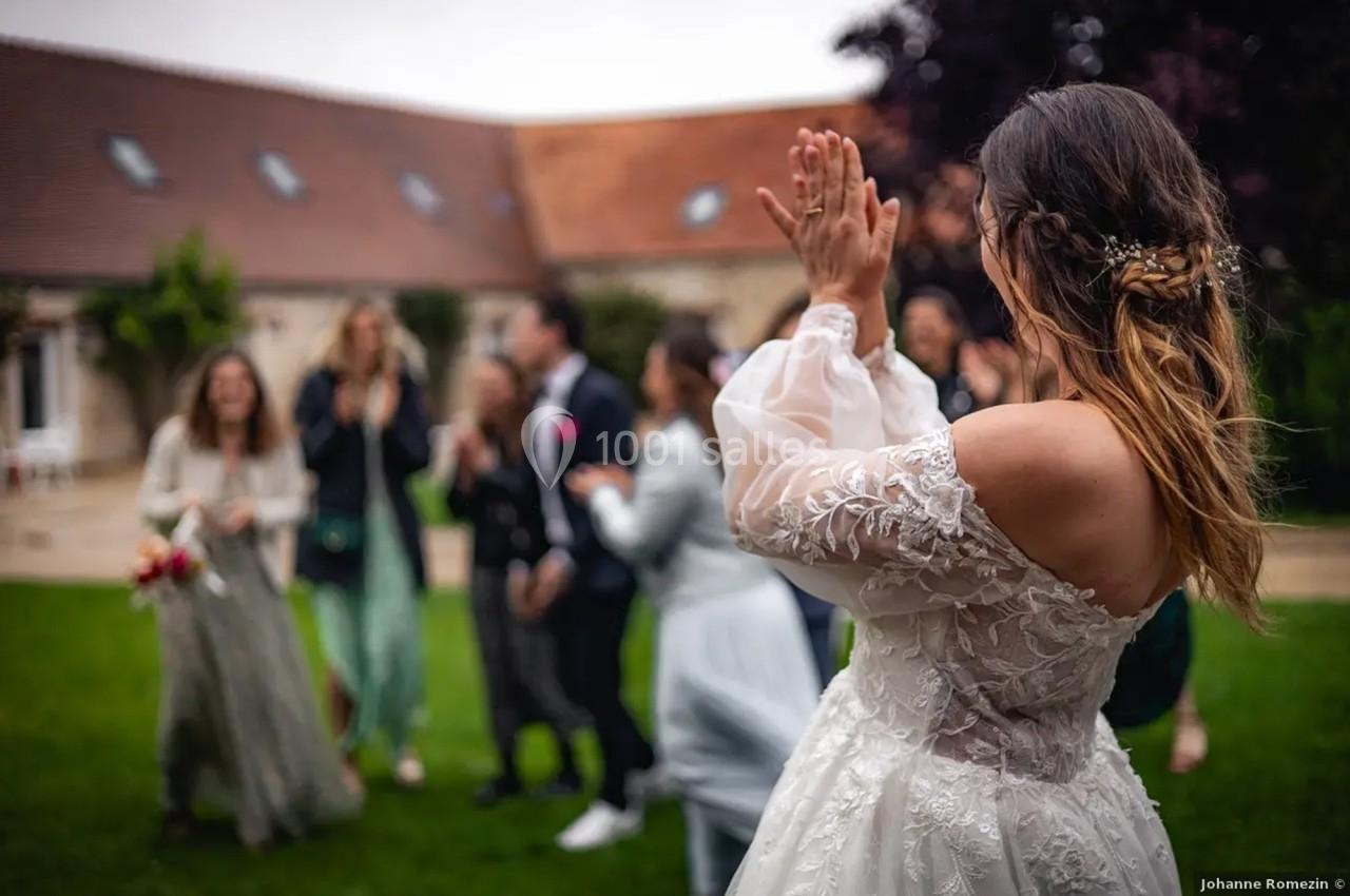 Location salle La Chapelle-Gauthier (Seine-et-Marne) - Nomade-Lodge #77 Une mariée en robe blanche applaudit devant un groupe de personnes dans un jardin lors d'une célébration.