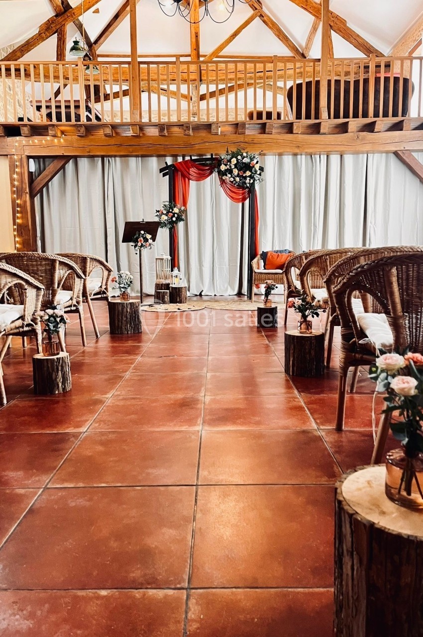 Salle de réception rustique avec chaises en osier, décor floral et arche ornée de rideaux rouges et blancs.