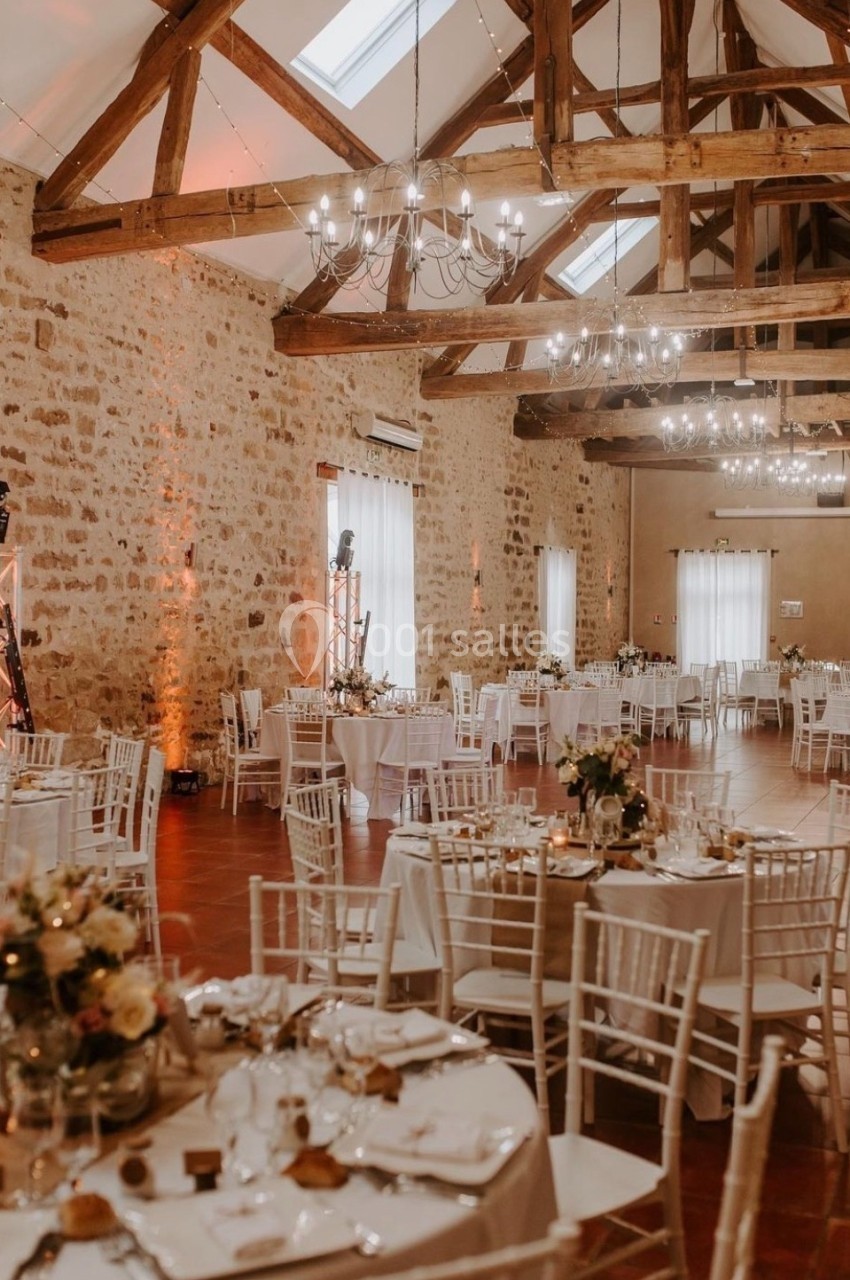 Salle de réception avec murs en pierre, poutres apparentes et tables rondes décorées pour un événement.