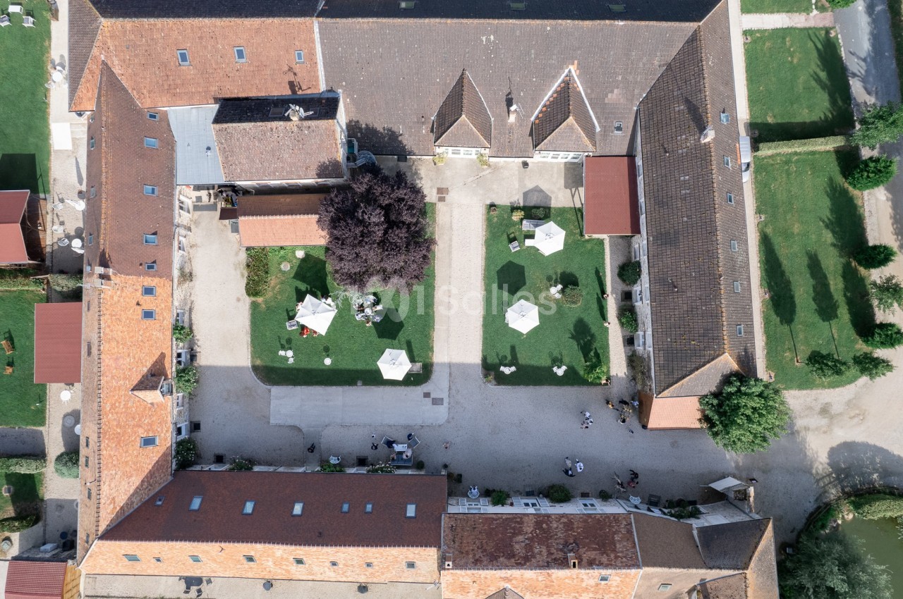 Vue aérienne d'une cour intérieure entourée de bâtiments en briques, avec des jardins et des tables équipées de parasols.