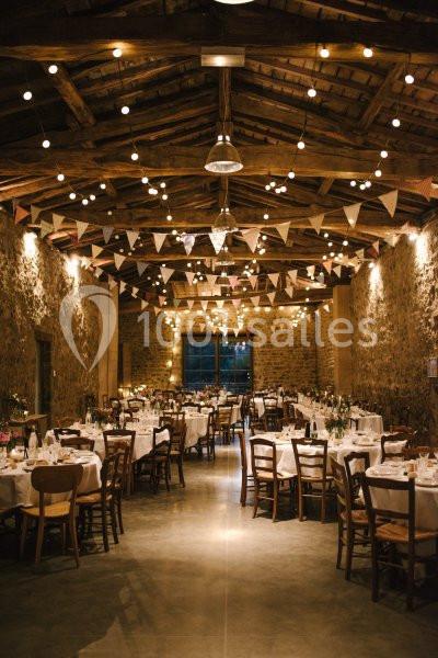 Salle de réception rustique décorée de guirlandes lumineuses et de fanions, avec des tables dressées pour un événement.