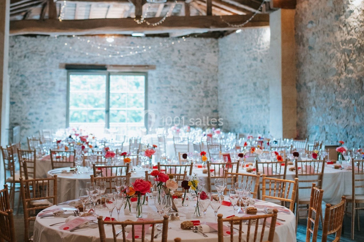 Salle de réception décorée avec des tables rondes, nappes blanches, chaises en bois et centres de table fleuris.