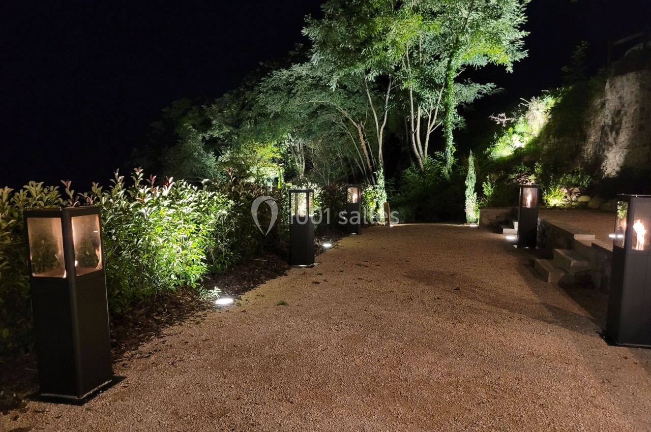 Allée extérieure éclairée la nuit par des lanternes modernes et des spots au sol, entourée de végétation.