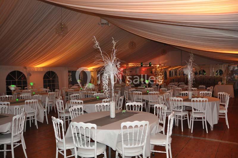 Salle de réception décorée avec des tables rondes, nappes blanches et centres de table ornés de branches blanches.