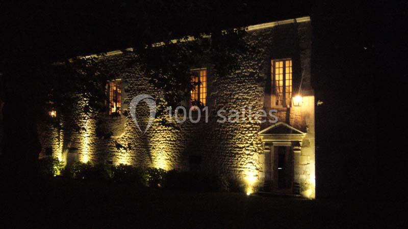 Façade en pierre d'un bâtiment éclairée par des lumières chaudes, avec des fenêtres illuminées la nuit.