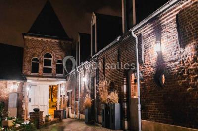 Salle de réception décorée avec des tables rondes dressées, des fleurs colorées et un mur de briques apparentes.