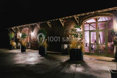 Salle de réception décorée avec des tables rondes dressées, des fleurs colorées et un mur de briques apparentes.