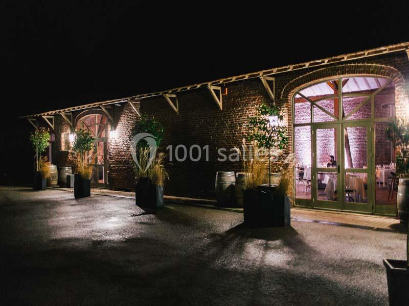 Façade en briques d'un bâtiment éclairé la nuit, avec de grandes portes vitrées et des plantes en pots.