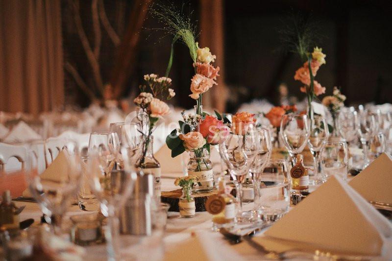 Table élégamment dressée avec des verres, serviettes pliées et bouquets de fleurs colorées en centre de table.
