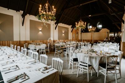 Salle de réception décorée avec des tables rondes dressées, des fleurs colorées et un mur de briques apparentes.