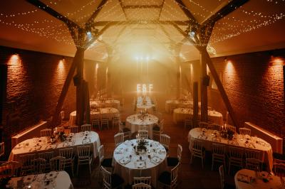 Salle de réception décorée avec des tables rondes dressées, des fleurs colorées et un mur de briques apparentes.