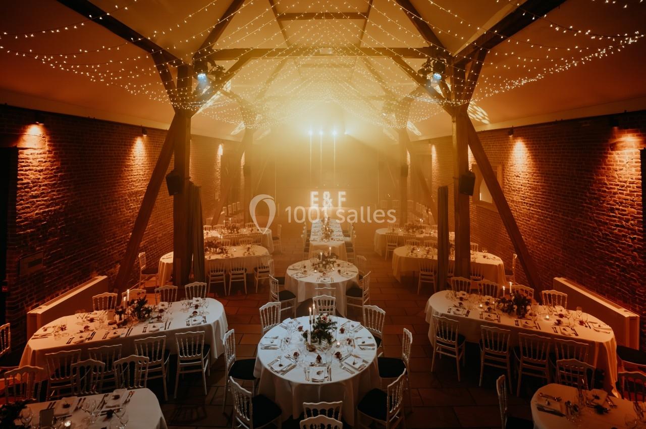 Salle de réception décorée avec des guirlandes lumineuses, tables rondes dressées et initiales éclairées en arrière-plan.