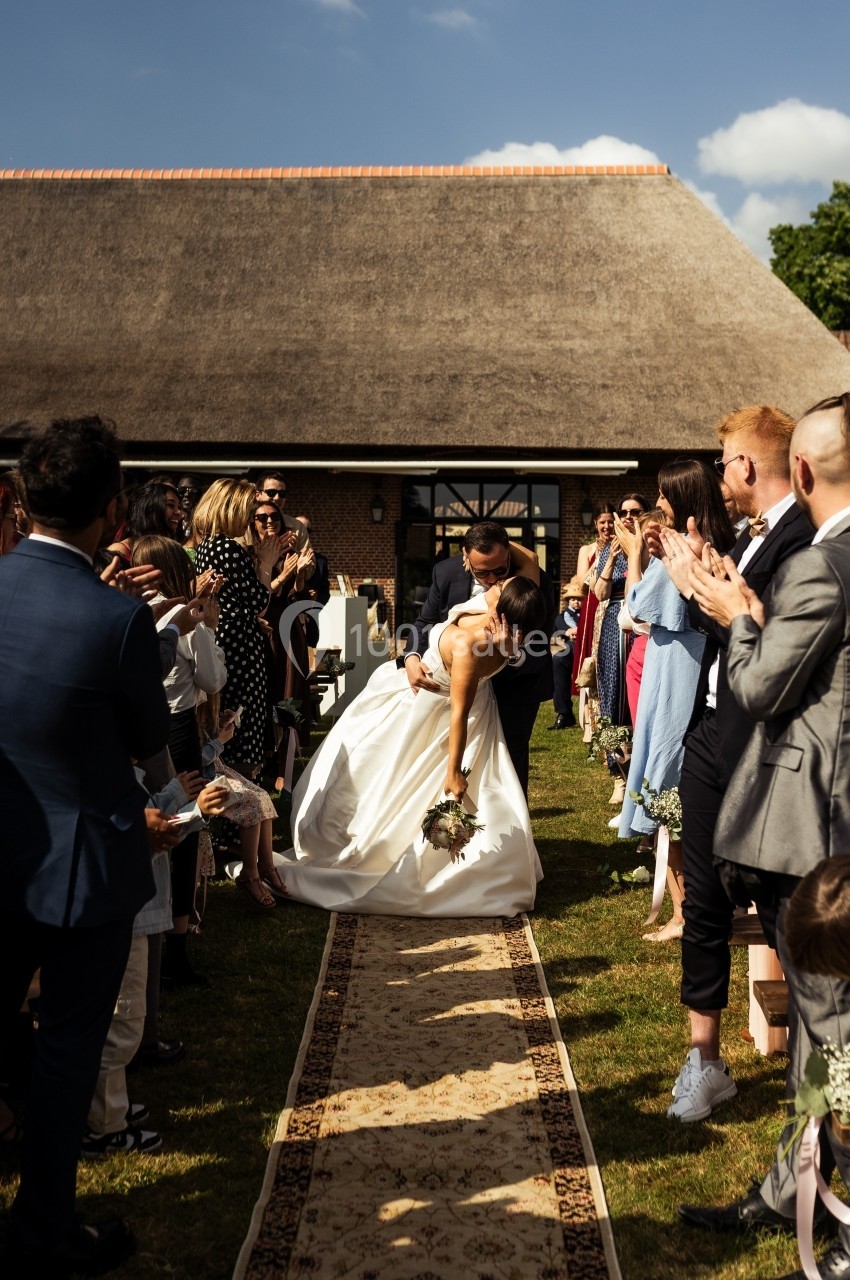 Un couple de mariés s'embrasse au milieu d'une allée extérieure, entouré d'invités applaudissant.
