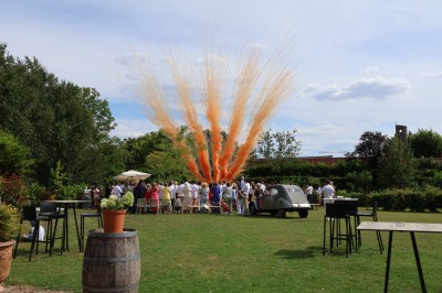Salle de réception décorée avec des tables rondes dressées, des fleurs colorées et un mur de briques apparentes.
