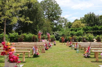 Salle de réception décorée avec des tables rondes dressées, des fleurs colorées et un mur de briques apparentes.