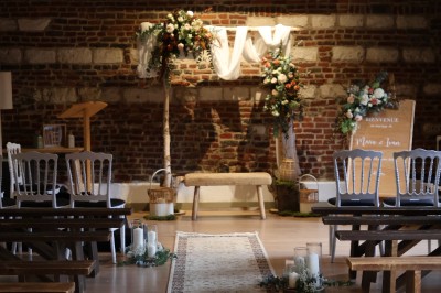 Salle de réception décorée avec des tables rondes dressées, des fleurs colorées et un mur de briques apparentes.