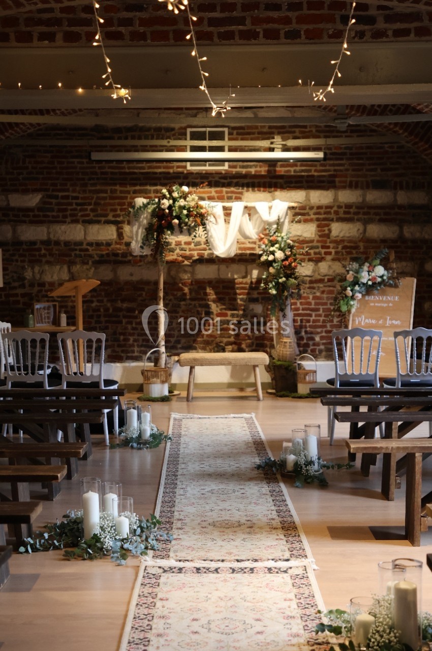 Allée centrale décorée de bougies et fleurs menant à un autel dans une salle en briques avec guirlandes lumineuses.