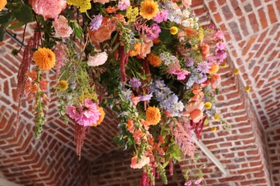 Salle de réception décorée avec des tables rondes dressées, des fleurs colorées et un mur de briques apparentes.