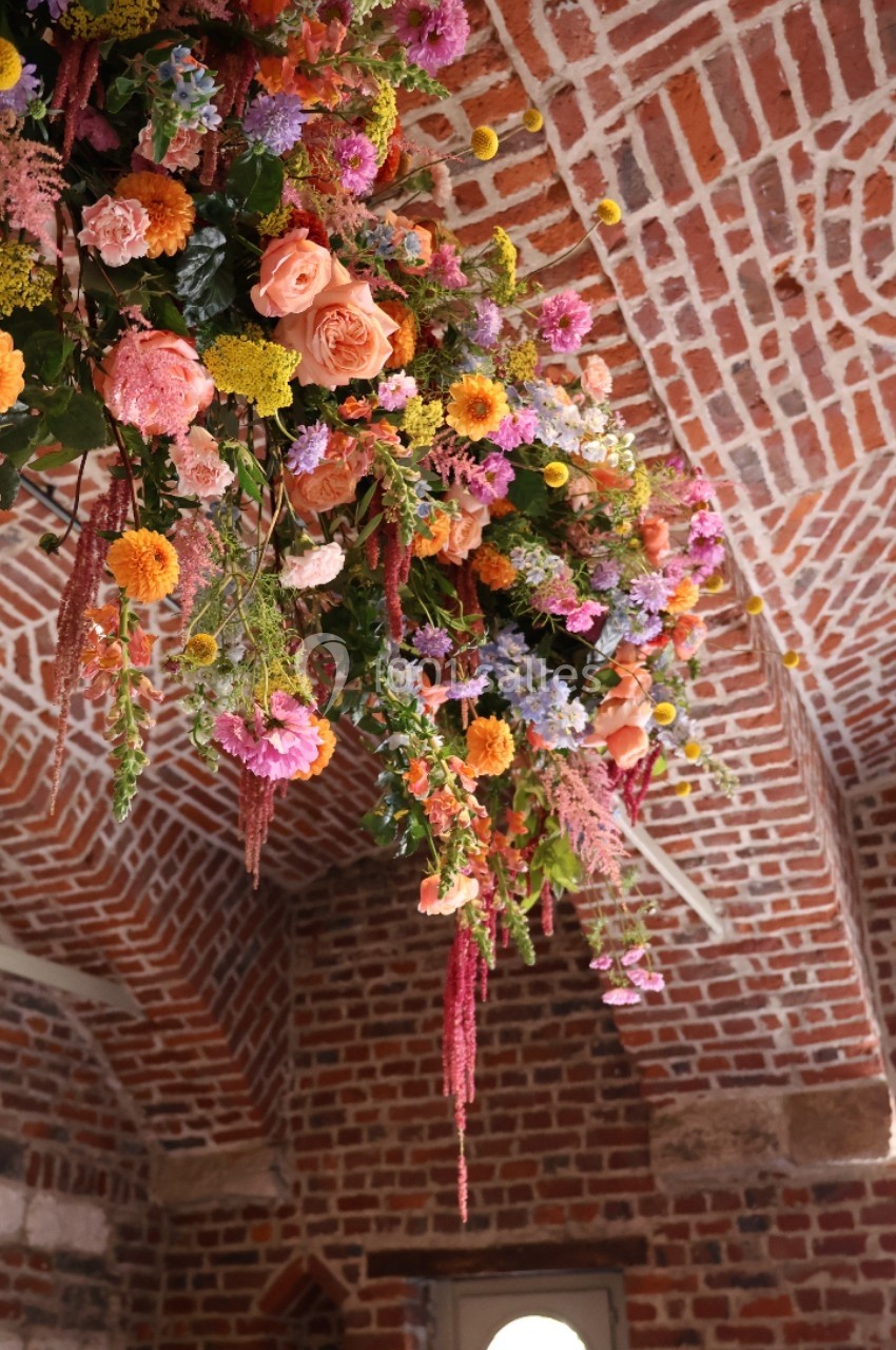 Suspension florale colorée avec des roses, des marguerites et des feuillages, accrochée sous une voûte en briques.