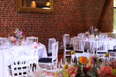 Salle de réception décorée avec des tables rondes dressées, des fleurs colorées et un mur de briques apparentes.