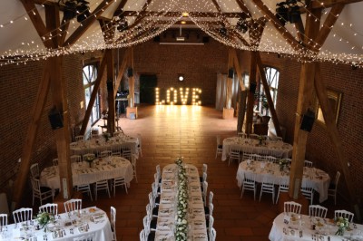 Salle de réception décorée avec des tables rondes dressées, des fleurs colorées et un mur de briques apparentes.