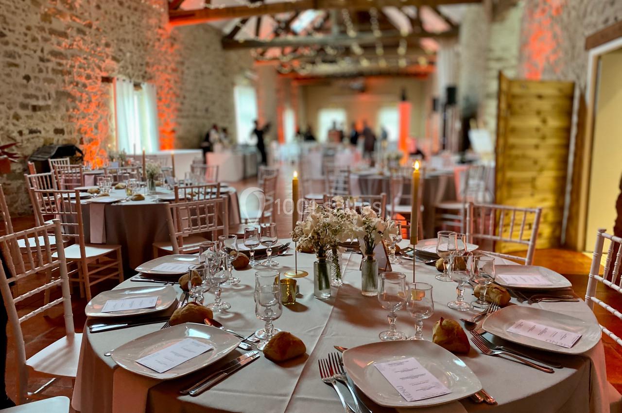 Salle de réception décorée avec des tables rondes dressées, bougies allumées et éclairage chaleureux.