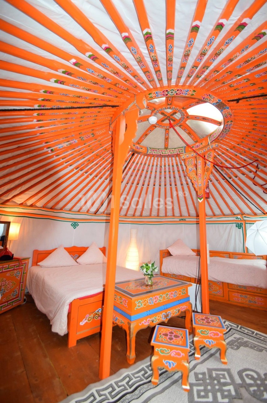 Intérieur d'une yourte traditionnelle avec lits, mobilier en bois peint et décorations colorées sous une structure…