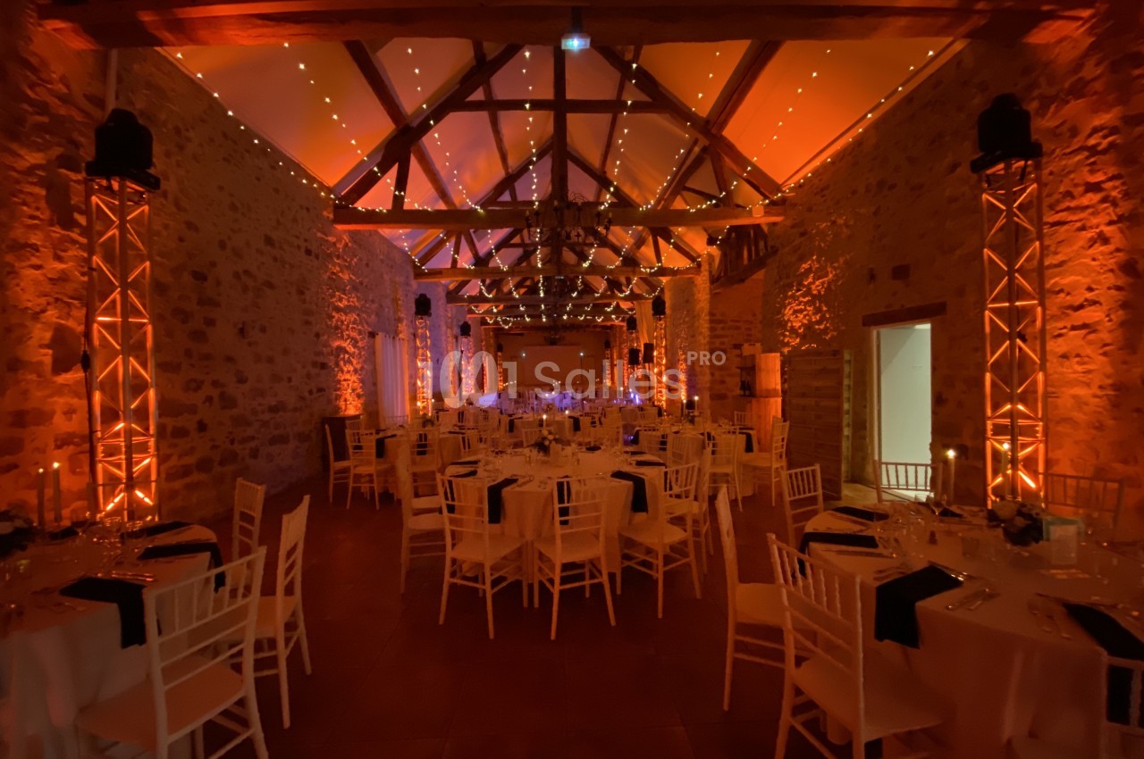 Salle de réception en pierre avec tables dressées, éclairage chaleureux et poutres apparentes au plafond.