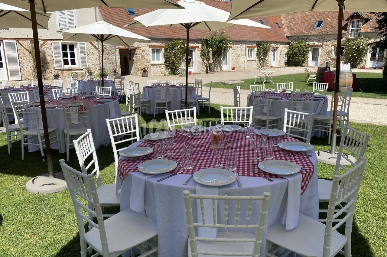 Tables rondes dressées avec nappes à carreaux rouges et blanches, disposées en extérieur sous des parasols.