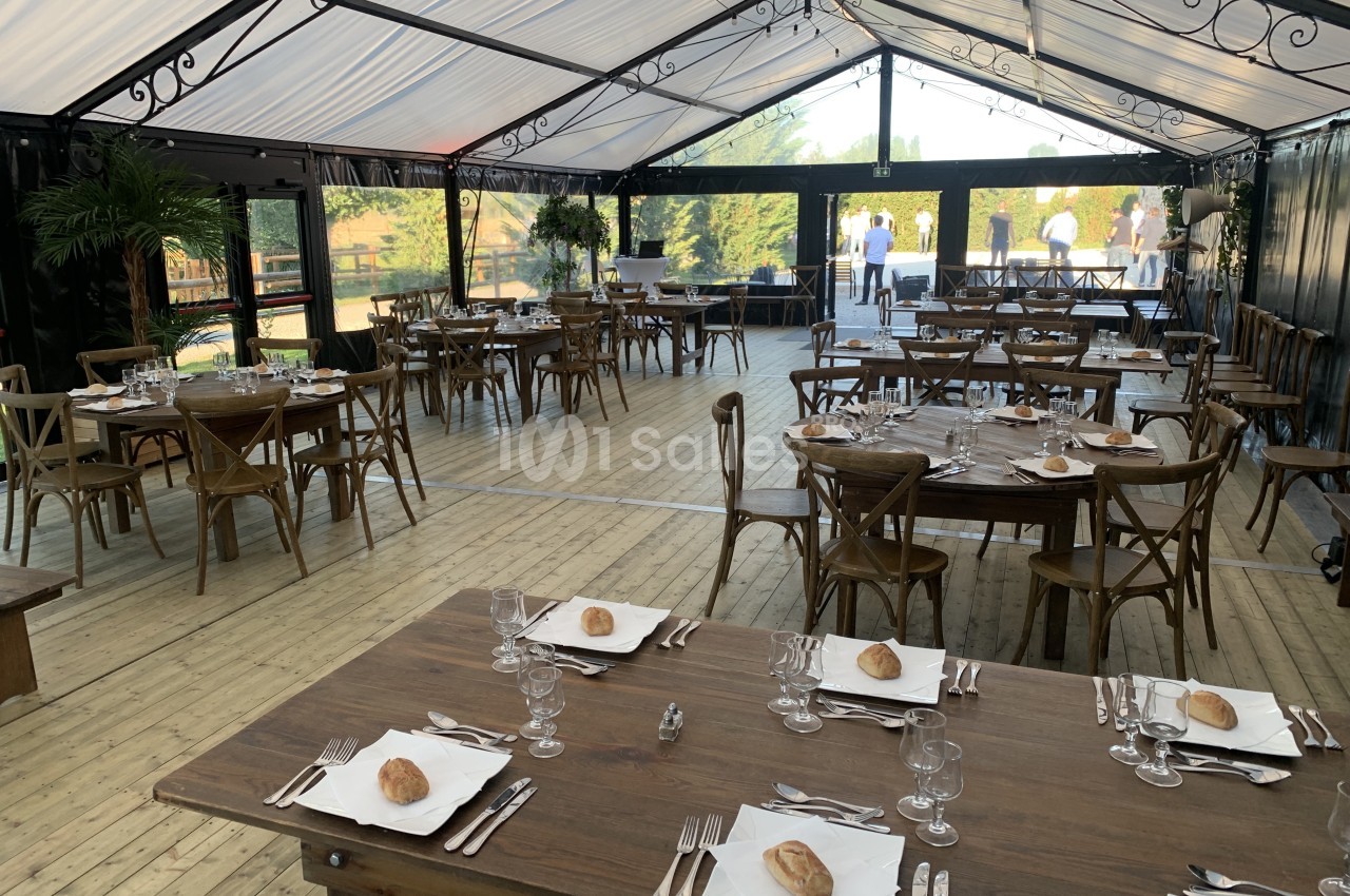 Salle de réception avec tables en bois dressées, couverts disposés et vue sur l'extérieur à travers des parois vitrées.
