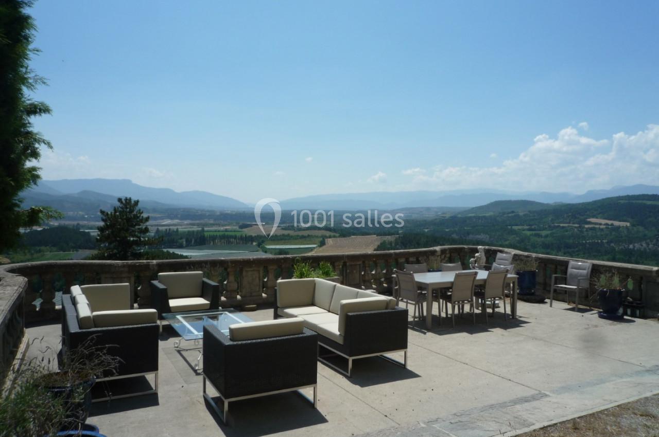 Terrasse meublée avec vue panoramique sur une vallée verdoyante et des collines sous un ciel dégagé.