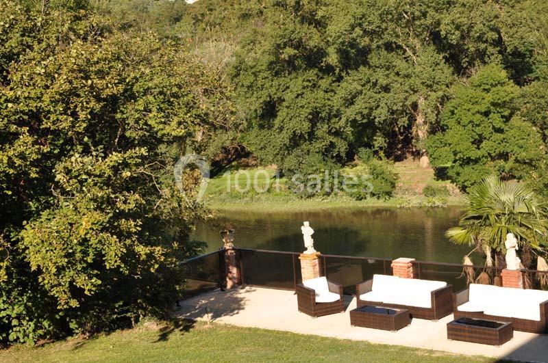 Terrasse avec mobilier en rotin, bordée d'arbres et surplombant une rivière entourée de végétation dense.