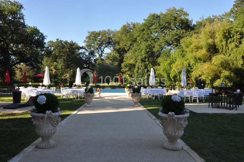 Allée centrale menant à une piscine entourée de tables blanches, parasols et végétation luxuriante.