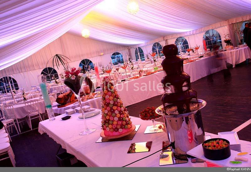 Buffet de desserts dans une tente éclairée, avec fontaine de chocolat et pièce montée de macarons au premier plan.