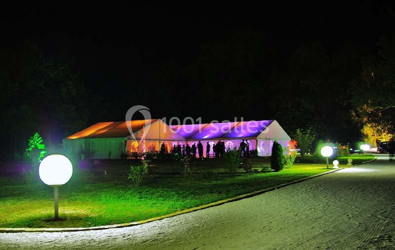 Grande tente éclairée de lumières colorées dans un jardin la nuit, avec des lampes sphériques le long d'une allée.
