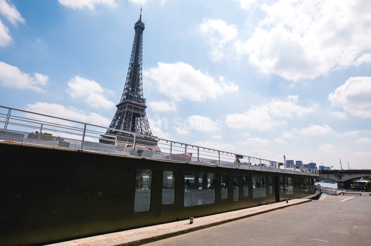 Vue de la tour Eiffel par une journée ensoleillée, avec une péniche amarrée au premier plan.