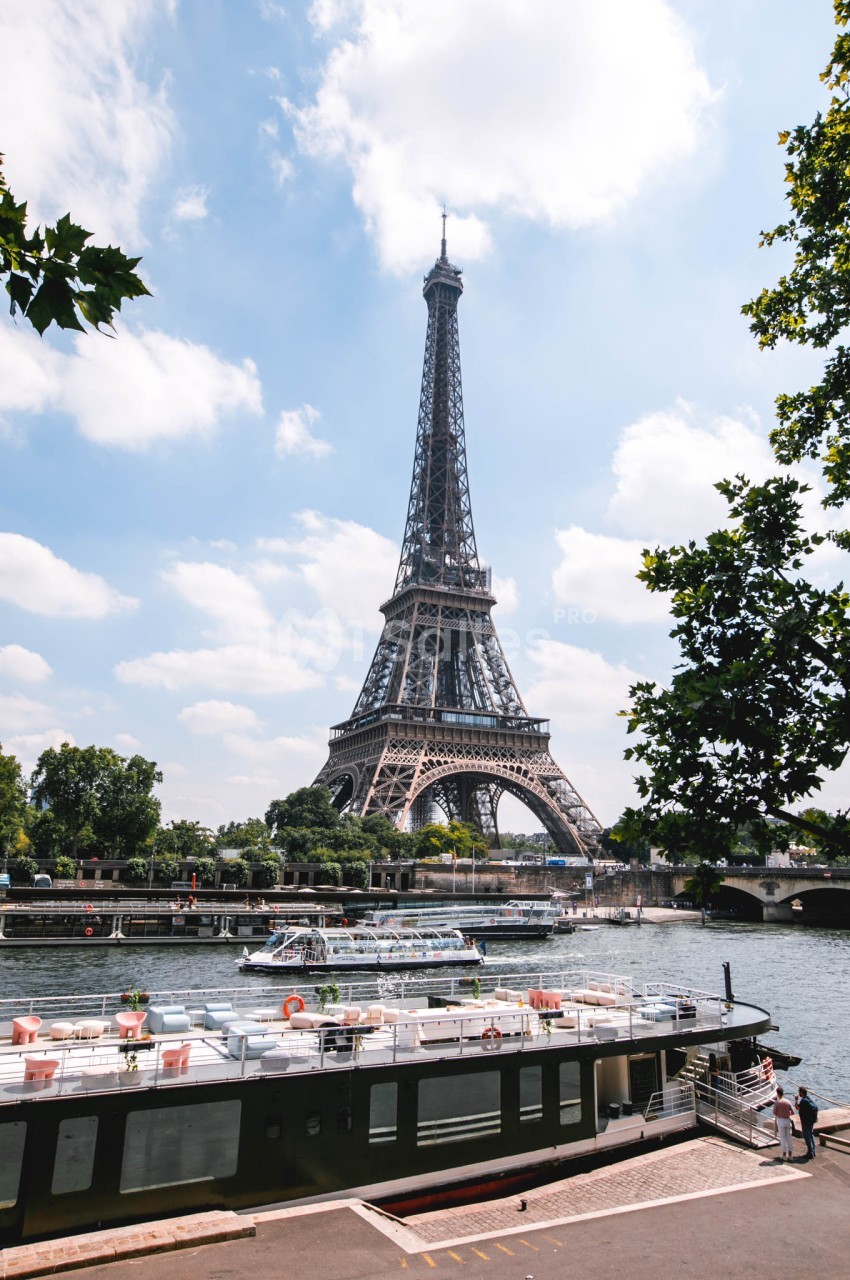 Vue de la tour Eiffel par une journée ensoleillée, avec des bateaux amarrés sur la Seine au premier plan.