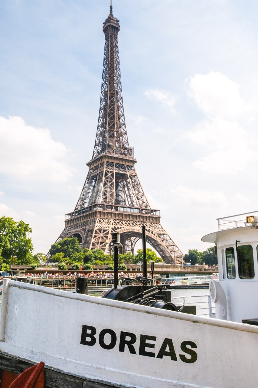 Vue de la tour Eiffel depuis la Seine avec une péniche blanche portant le nom ’Boreas’ au premier plan.