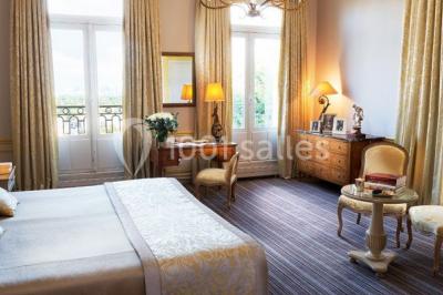 Deux tables de massage recouvertes de draps beiges, avec une vue sur un paysage urbain et verdoyant à travers une fenêtre.