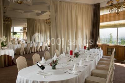 Deux tables de massage recouvertes de draps beiges, avec une vue sur un paysage urbain et verdoyant à travers une fenêtre.